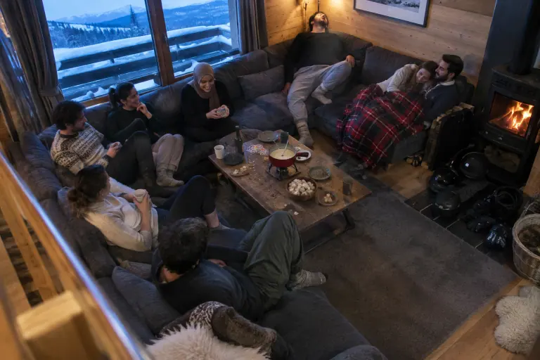 Dans un chalet savoyard à la tombée du jour, huit amis en chaussettes de laine jouent aux cartes sur un très grand canapé modulable en U gris anthracite