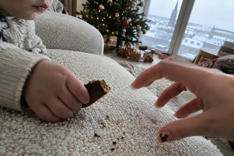 Gros plan sur l’assise d’un canapé en bouclette écrue où la main d’un adulte intercepte de justesse le biscuit au chocolat d’un tout-petit