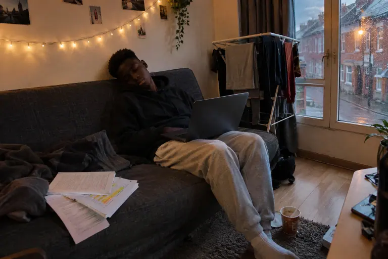Dans un studio étudiant à Lille, un jeune homme s’est endormi sur un clic-clac gris foncé, son ordinateur sur les genoux, un soir de pluie