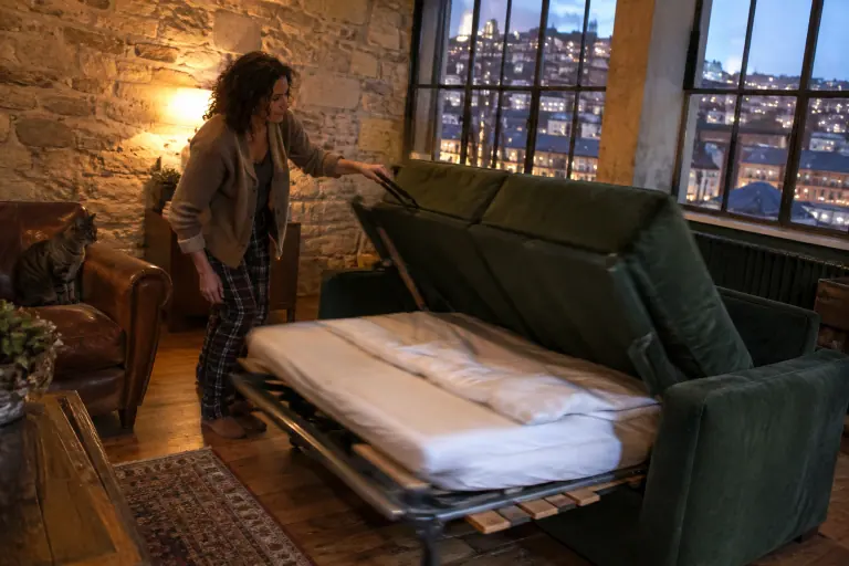 Une femme tire la sangle d’un canapé rapido vert sapin dont le matelas, déjà garni de draps, se déplie dans un loft lyonnais un soir d’automne