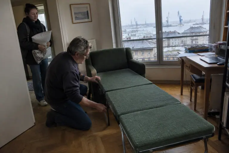 Dans un bureau d’appartement au Havre, un homme déplie un fauteuil lit vert bouteille pendant que sa fille étudiante attend avec un oreiller