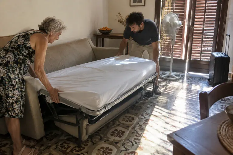 Une femme d’une soixantaine d’années et son fils déplient un canapé convertible express beige sable dans un appartement de Perpignan, volets mi-clos en été