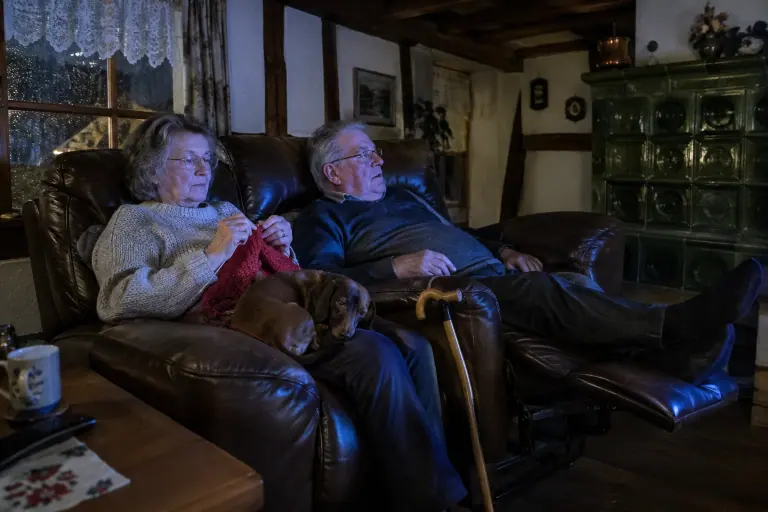 Un couple âgé regarde un match sur un canapé relax électrique 2 places en cuir chocolat, repose-pieds levé, dans une maison à colombages près de Colmar